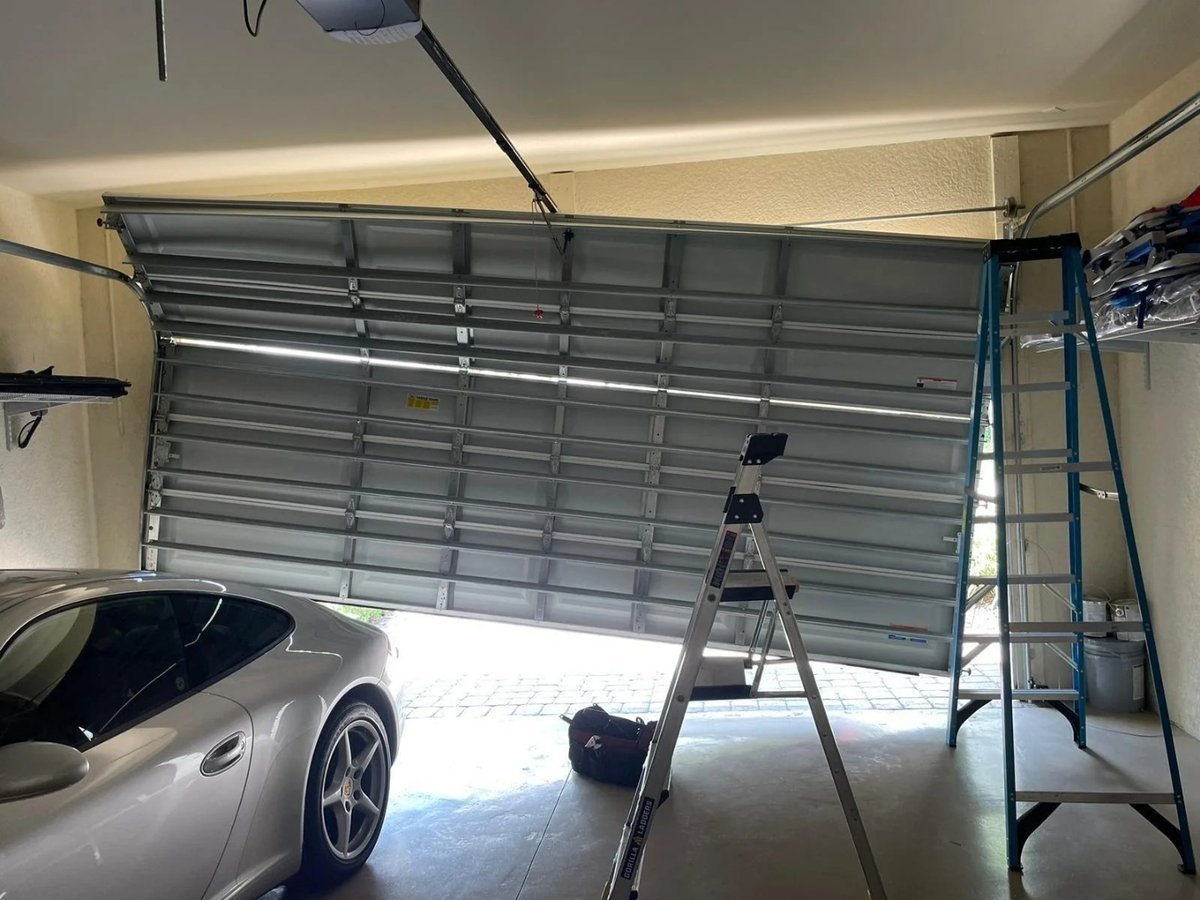 Garage door hanging crooked off its track above a parked silver car