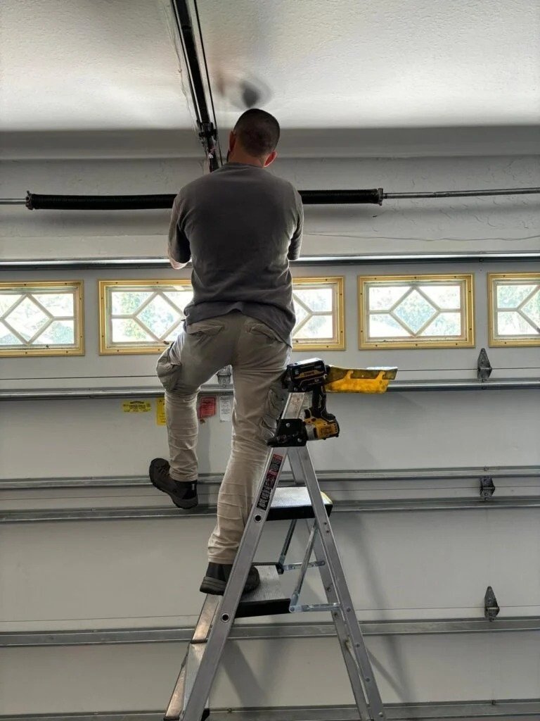 Technician on a ladder reaching the top section of a white door with window inserts