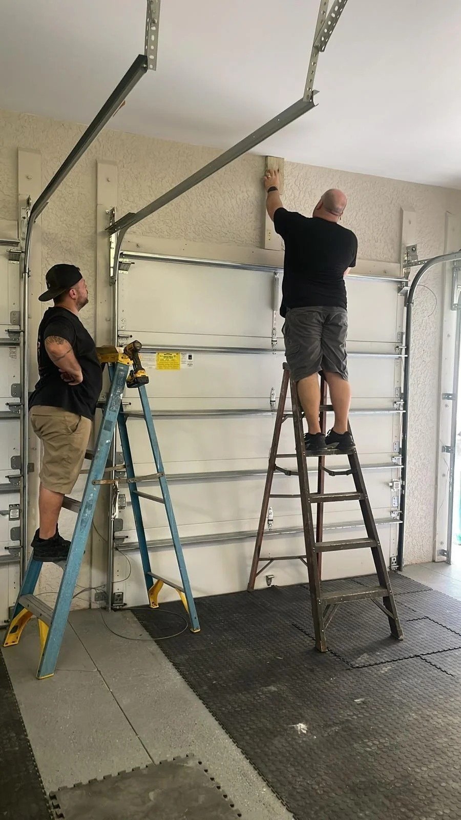 Two installers on ladders fitting a new white garage door