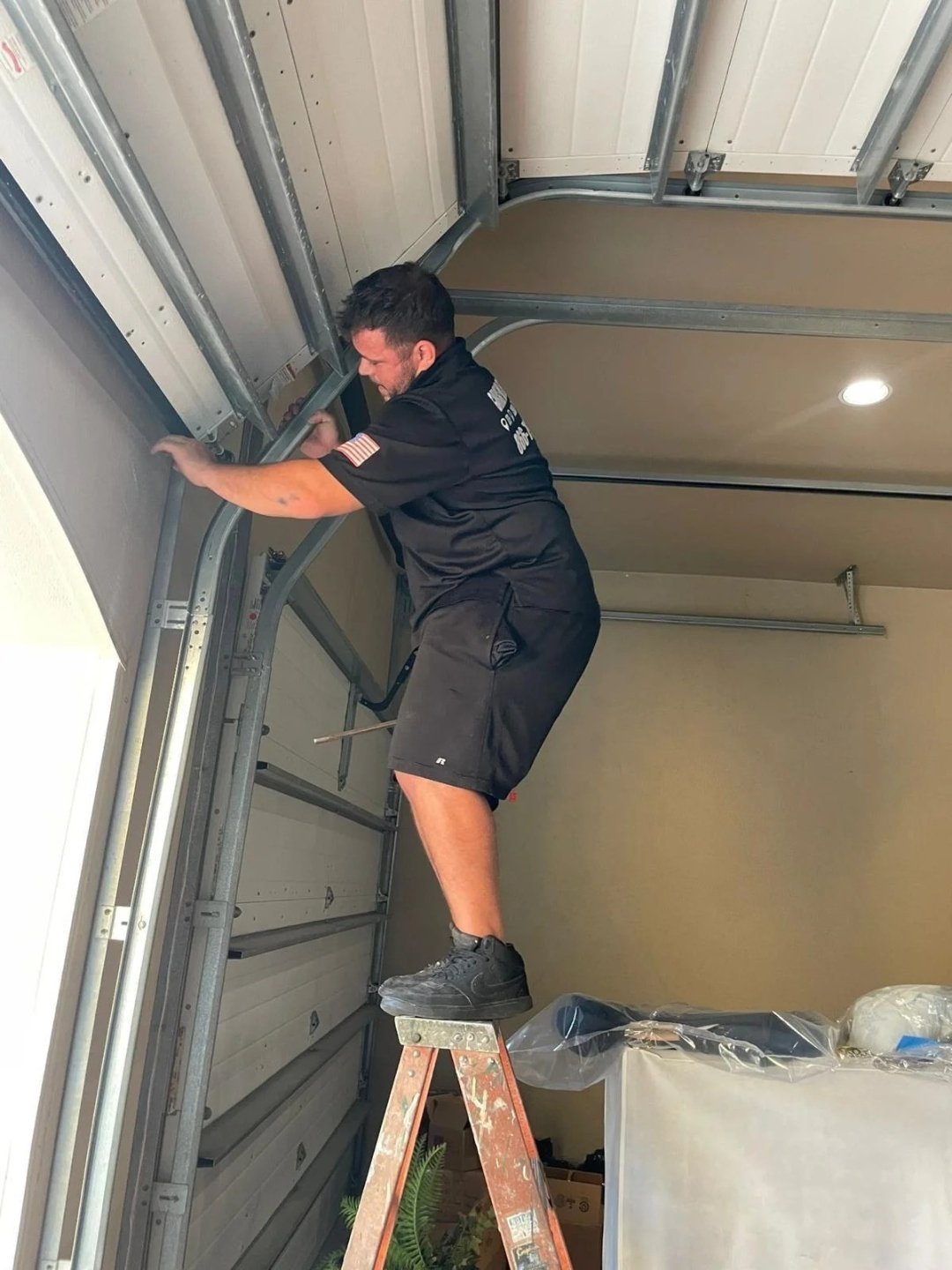 Technician on a step ladder adjusting the vertical track beside the door