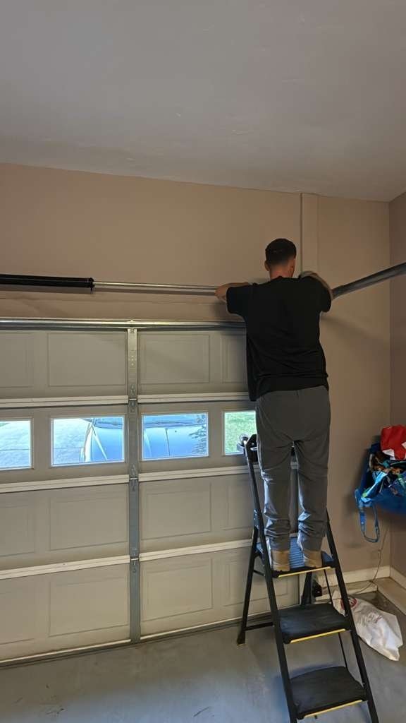 Technician on a ladder working above a white door with a row of windows