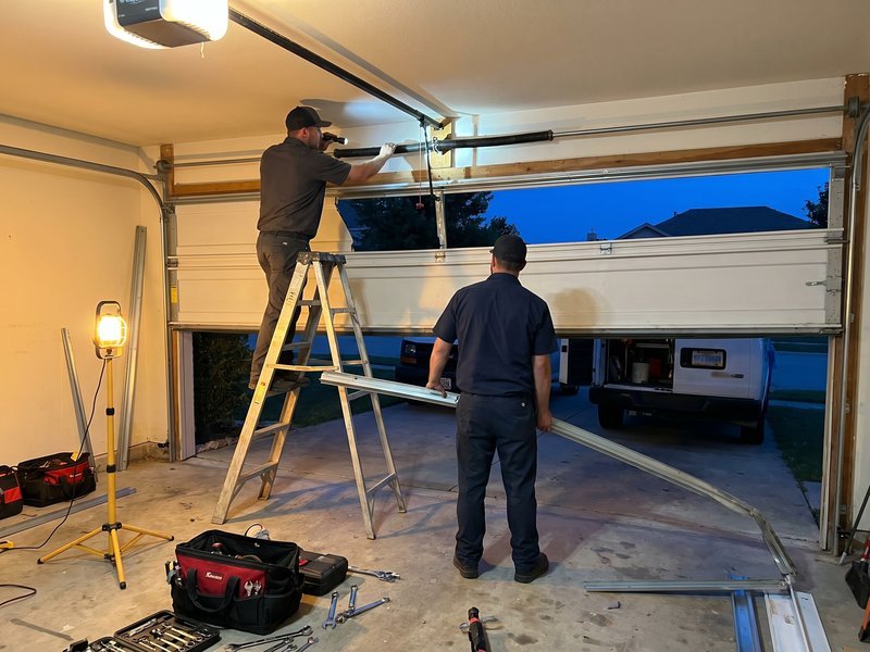 Technicians fitting a garage door from inside the garage, one on a ladder